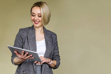 Glückliche reife Geschäftsfrau mit blondem Haar, die ein digitales Tablet vor einer Wand benutzt - OGF01053