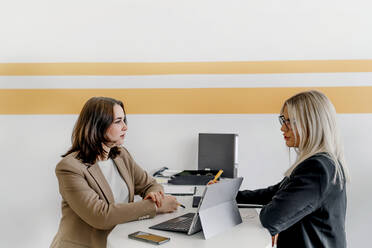 Junge Kolleginnen diskutieren zusammen am Schreibtisch sitzend im Büro - OGF01058