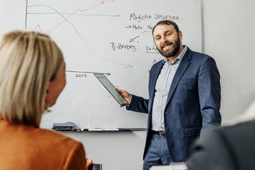 Lächelnder Geschäftsmann, der eine weibliche Kollegin anschaut, während er bei einer Besprechung im Büro eine Strategie diskutiert - OGF01070