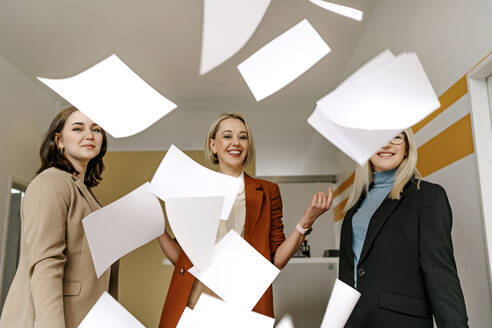 Glückliche Geschäftsfrauen, die Dokumente werfen und sich im Büro zusammen vergnügen - OGF01078