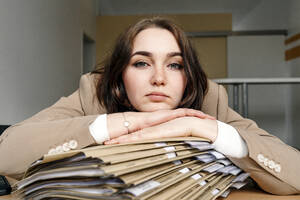 Junge Geschäftsfrau stützt sich auf einen Aktenstapel am Schreibtisch im Büro - OGF01084