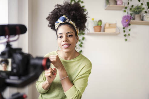 Young woman wearing headband filming through camera at home - JCCMF03134