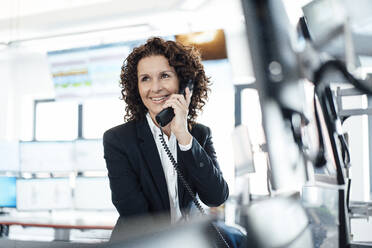 Smiling businesswoman talking on landline telephone in control room - MOEF03738