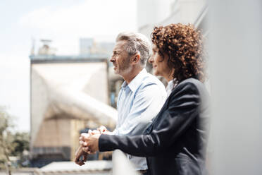 Thoughtful businessman standing with colleague by railing - MOEF03748