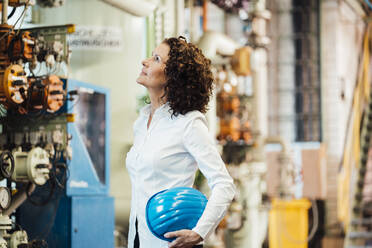 Female engineer holding hardhat while checking machine at power station - MOEF03786