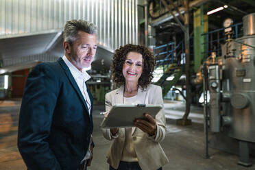 Fröhliche Geschäftsfrau zeigt einem Kollegen in der Industrie ein digitales Tablet - MOEF03812