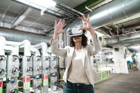 Businesswoman using virtual reality headset while standing in workshop - MOEF03830