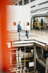 Male and female colleagues having discussion while standing in industry - MOEF03836