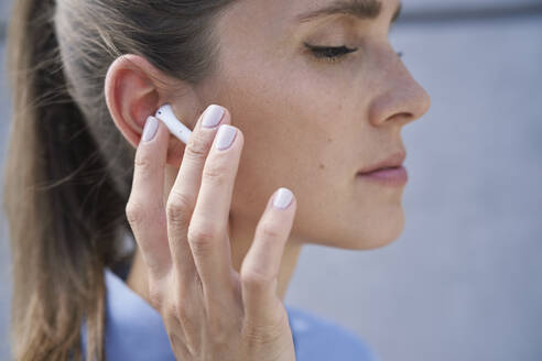 Businesswoman touching wireless in-ear headphones - ABIF01408