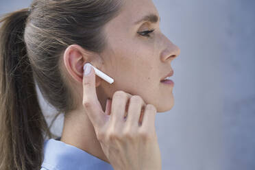 Geschäftsfrau mit drahtlosen In-Ear-Kopfhörern an der Wand - ABIF01409