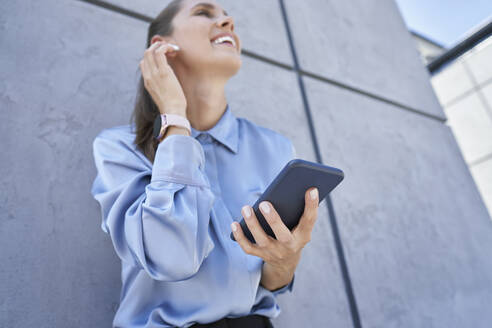Geschäftsfrau, die ein Mobiltelefon hält, während sie vor einer Wand steht - ABIF01413