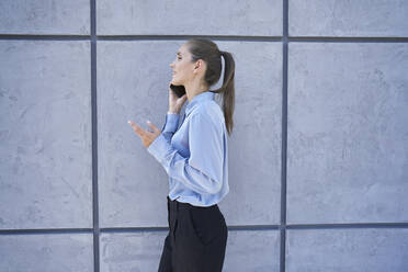 Businesswoman talking on mobile phone while walking by wall - ABIF01419