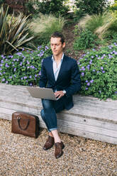 Businessman using laptop while sitting in park - ASGF00806