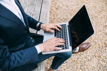 Businessman using laptop while sitting at park - ASGF00808