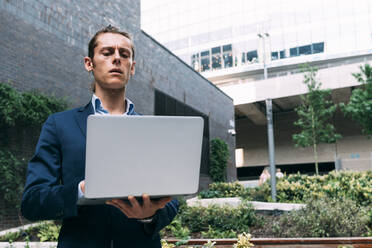 Businessman using laptop while standing in park - ASGF00815