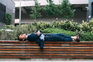 Businessman with laptop relaxing on bench at park - ASGF00817