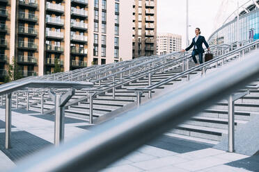 Geschäftsmann mit Aktenkoffer, der sich auf einer Treppe in der Stadt nach unten bewegt - ASGF00849