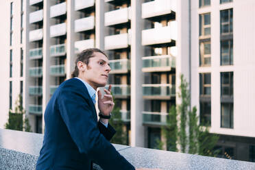 Thoughtful businessman leaning on retaining wall - ASGF00851