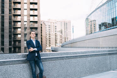 Businessman with arms crossed leaning on retaining wall - ASGF00852