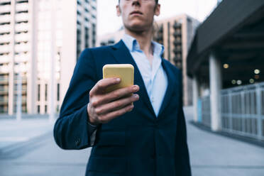 Geschäftsmann, der ein Mobiltelefon benutzt, während er auf dem Gehweg steht - ASGF00853