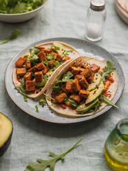 Von oben Tortillas mit gebratenen Tofuwürfeln und Avocadostücken mit frischen Rucolablättern auf dem Tischtuch - ADSF27053