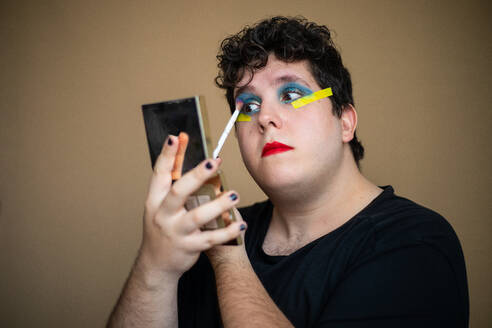 Auftragen von leuchtendem Make-up auf die Augenlider eines queeren Mannes - ADSF27056