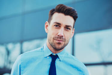 Bearded male executive in formal shirt and tie in city looking at camera on blurred background - ADSF27078