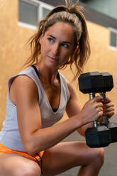 Fokussierte schlanke Sportlerin beim Kniebeugen mit schweren Hanteln während des Trainings im Fitnessstudio - ADSF27085