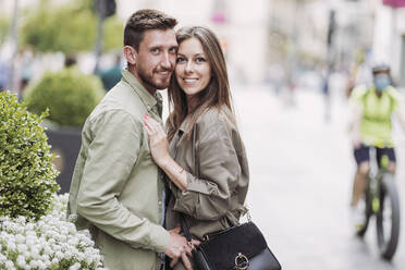 Smiling couple embracing while standing by flowers - LJF02252