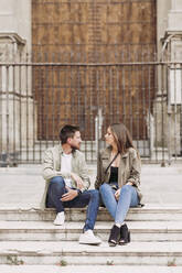 Mid adult couple talking while sitting on steps - LJF02260