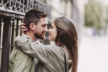 Mid adult couple rubbing noses while leaning on fence - LJF02263