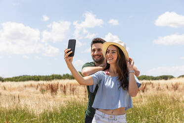 Lächelnde Frau nimmt Selfie mit Freund durch Smartphone auf sonnigen Tag - EIF01625