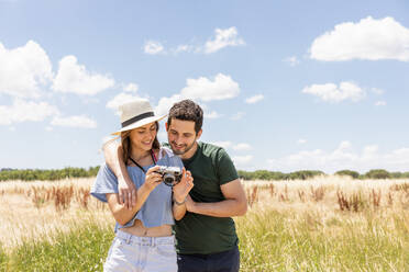 Frau mit Hut zeigt ihrem Freund die Kamera, während sie auf einer Wiese steht - EIF01627