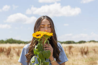 Junge Frau riecht an Sonnenblumen an einem sonnigen Tag - EIF01633