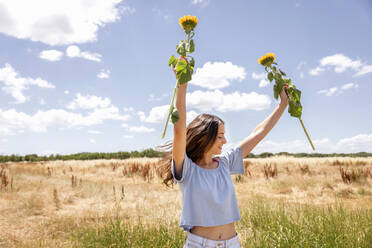Frau hält Sonnenblumen, während sie im Sommer auf einer Wiese steht - EIF01636