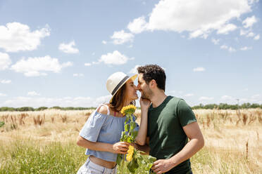 Lächelndes Paar mit Sonnenblumen, das sich an einem sonnigen Tag die Nasen reibt - EIF01637