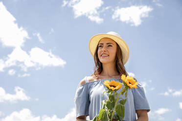 Junge Frau mit Hut und Sonnenblumen in der Hand an einem sonnigen Tag - EIF01640