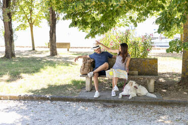 Touristenpaar mit Landkarte und Rucksack sitzt mit Hund auf einer Bank - EIF01650