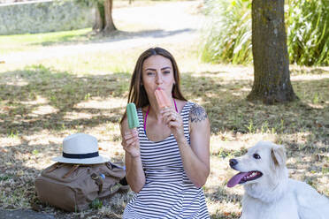 Woman eating ice cream while sitting by dog - EIF01665