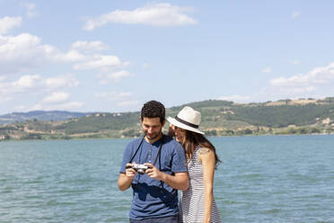 Paar überprüft Kamera, während es an einem sonnigen Tag am See steht - EIF01675