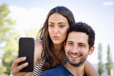 Frau knutscht, während sie ein Selfie mit ihrem Freund über ihr Smartphone macht - EIF01685