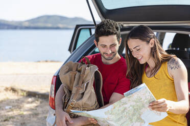 Boyfriend holding backpack while checking map with girlfriend during road trip - EIF01692