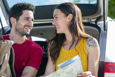 Smiling girlfriend looking at boyfriend while sitting in car trunk - EIF01693