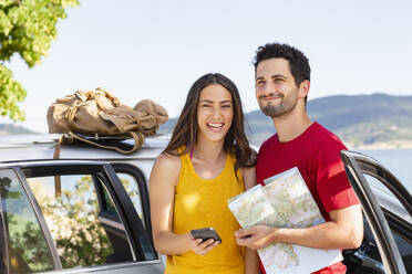 Glückliches Paar mit Landkarte und Mobiltelefon am Auto - EIF01698