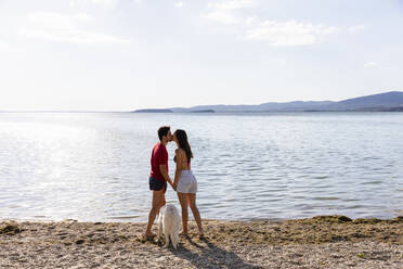 Couple kissing each other while standing by pet at lakeshore - EIF01707