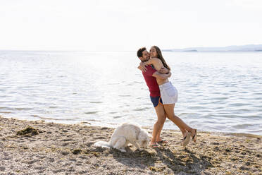Freund trägt seine Freundin beim Umarmen durch einen Hund am Seeufer - EIF01708