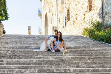 Man with arm around girlfriend sitting with dog on steps - EIF01727