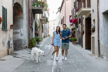 Smiling couple standing with dog on footpath in town - EIF01741