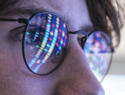 Männlicher Teenager-Wissenschaftler mit DNA-Testergebnissen, die auf einer Brille reflektiert werden - ABRF00902