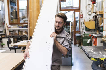 Männlicher Handwerker trägt ein weißes Brett in der Werkstatt - MEUF03553